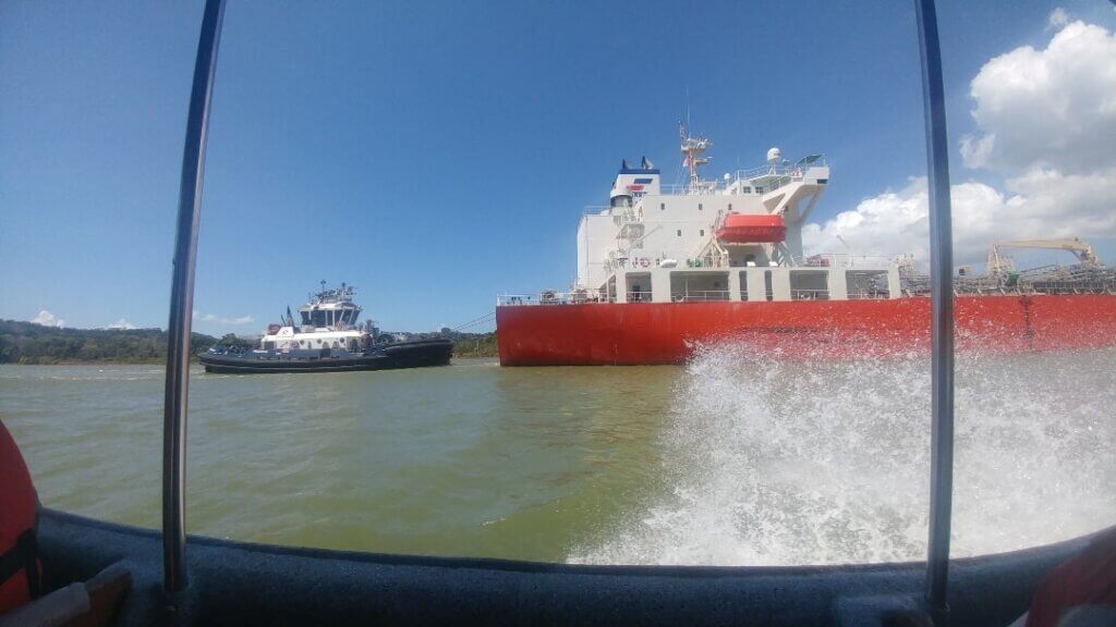 A smaller ship is helping a larger vessel navigate the Panama Canal 
