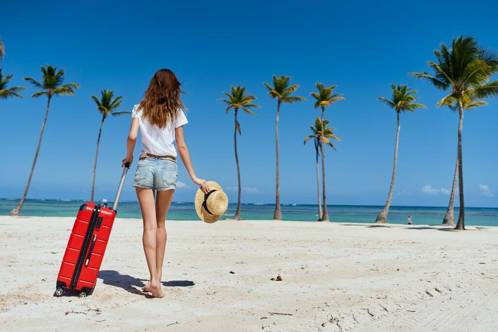A girl with a red luggage on a beach, Caribbean, is it safe to travel to the Dominican Republic 