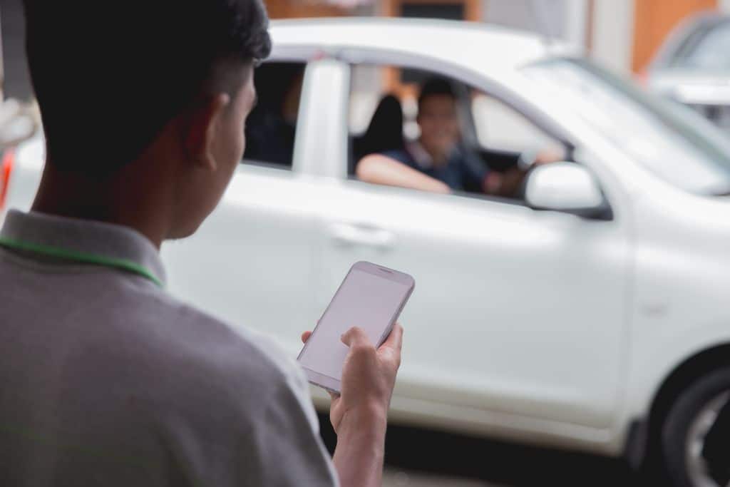 A person ordering an Uber, a white car in the background, a man holding a cell phone