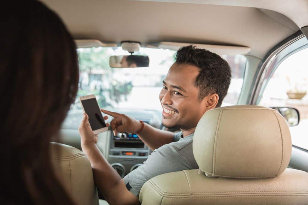 A man in the driving seat of a car holding a phone, Uber driver in a car