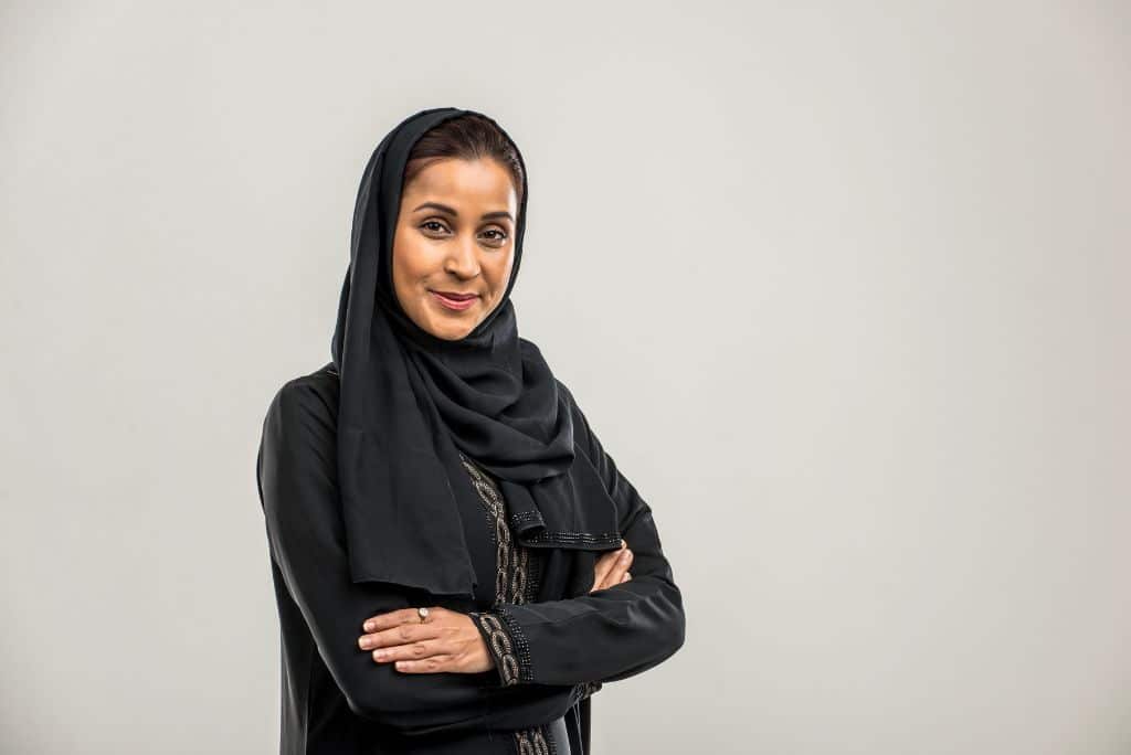 An arab woman standing with crossed arms and looking at the camera, white background