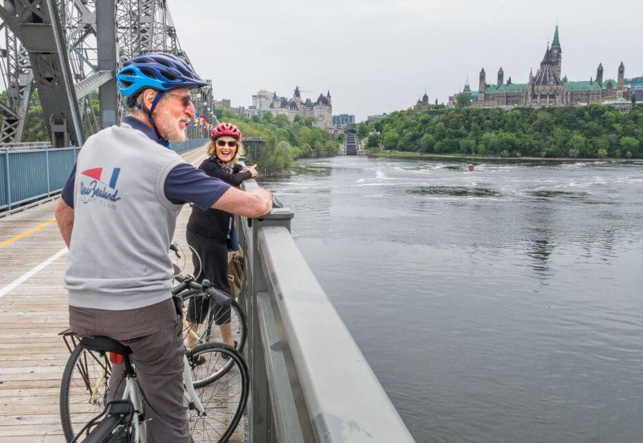 An older couple on a bridge biking beside a river, Ottawa biking, Ottawa Bike Tours, Ottawa bike rental 