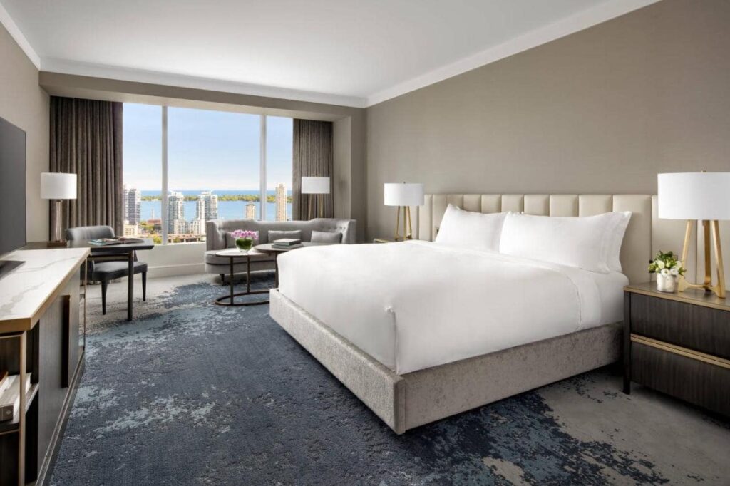 A room in the Ritz-Carlton, Toronto, a large hotel bed with white sheets, a window with a view