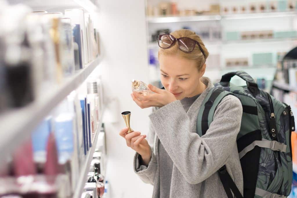A young white woman in an airport sniffing a perfume inside one of the duty free stores, walk through the duty-free shops, even if you’re not looking to buy anything