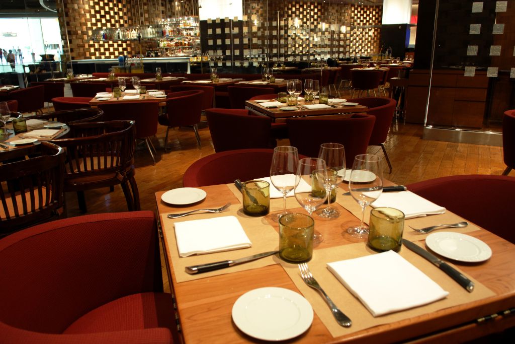 Tables in a restaurant with dishes and glasses, restaurant in an airport; instead of settling for a soggy sandwich or overpriced bag of chips from a convenience kiosk, use the extra time to treat yourself to a proper meal