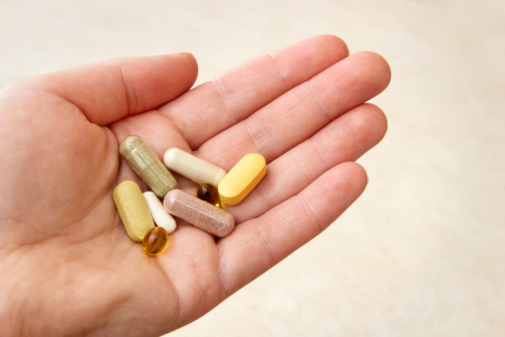 A close up of a hand, holding different vitamins, one of the essential travel medications that you need to bring are vitamins 