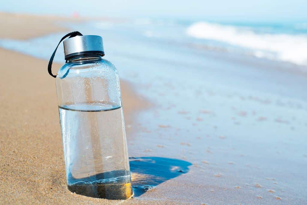 A see through water bottle on a beach, staying hydrated is one of the most important (and most overlooked) parts of spending a day in the sun