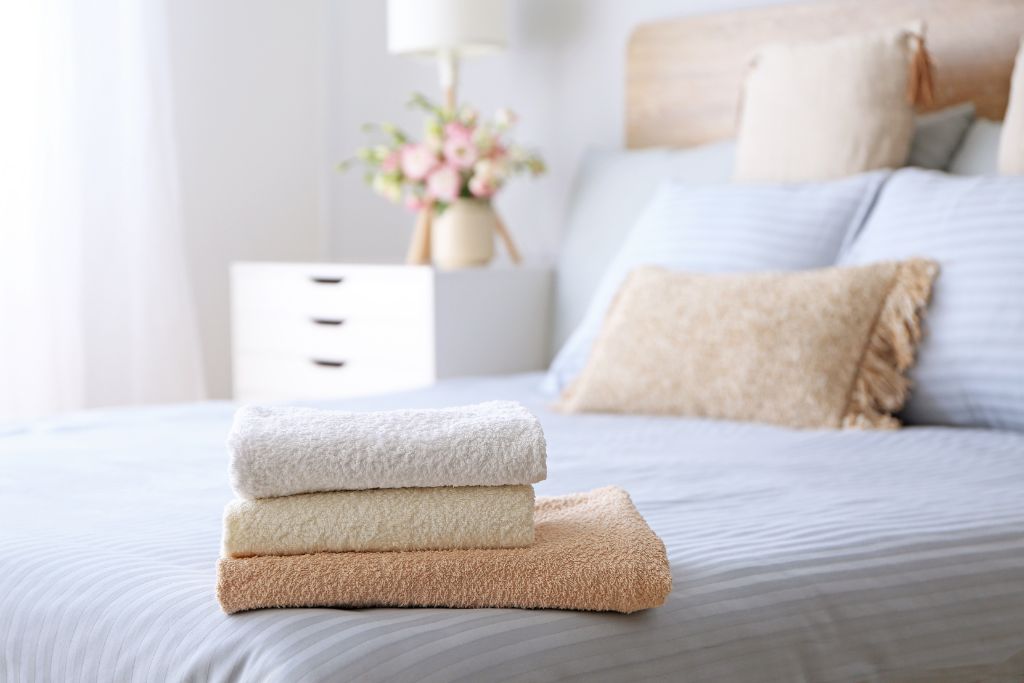 Three towels on a bed with white sheets, the towels are beige