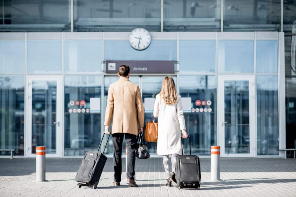 A white couple entering an airport with their luggage, they are both wearing coats 