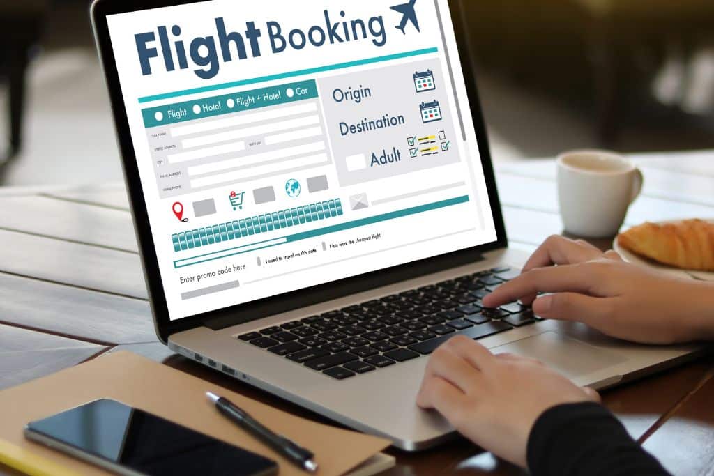A person typing on a laptop, the screen shows a website that says flight booking, one of the tips of how to travel more for less is to compare prices across multiple platforms before booking anything