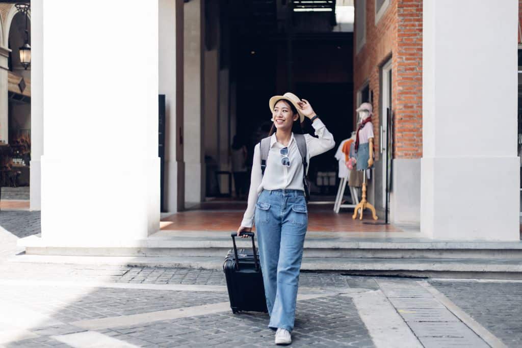 A young Asian woman with a small luggage walking around a city, single woman traveling