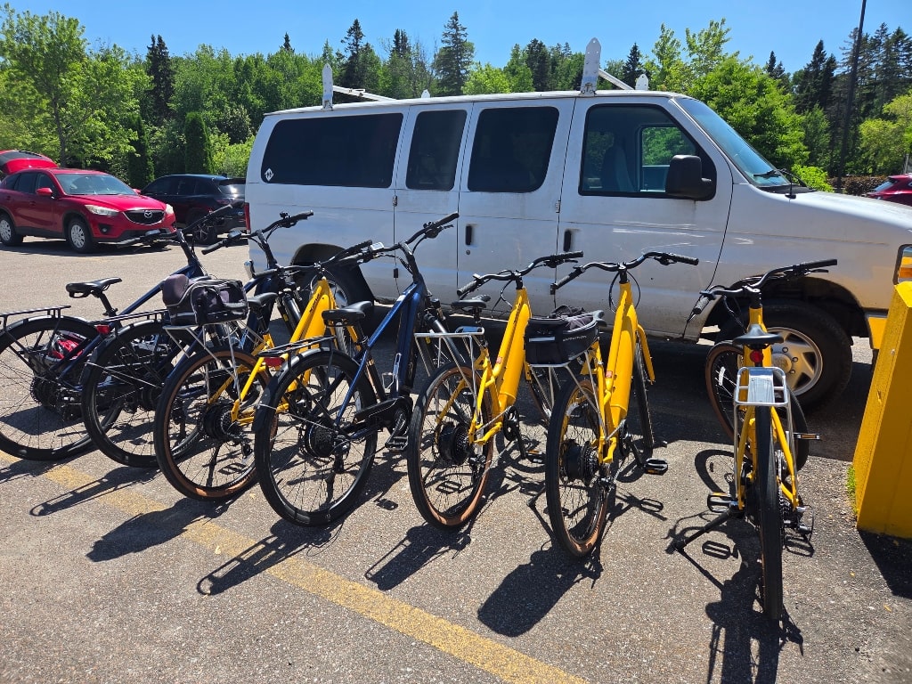 E-bikes parked in a line in a parking lot, yellow e-bikes, dark blue e-bikes, Is The Saguenay-Lac-Saint-Jean Region Of Quebec Worth Visiting?
