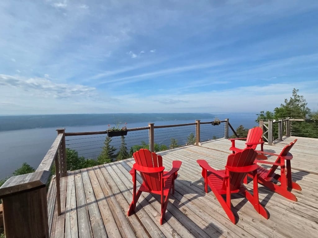 View of Fjord du Saguenay from the porch of Auberge Cap au Leste (hotel), 3 red Muskoka chairs on a deck