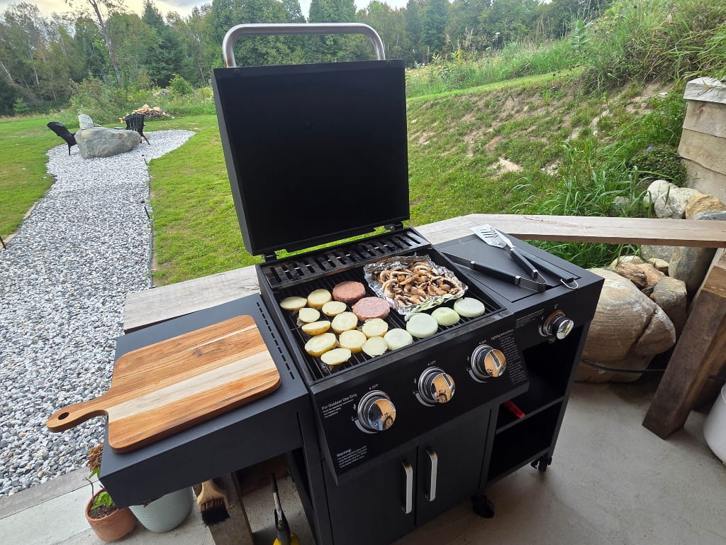 A BBQ with food cooking on it like potatoes, onions, mushrooms and veggie burgers
